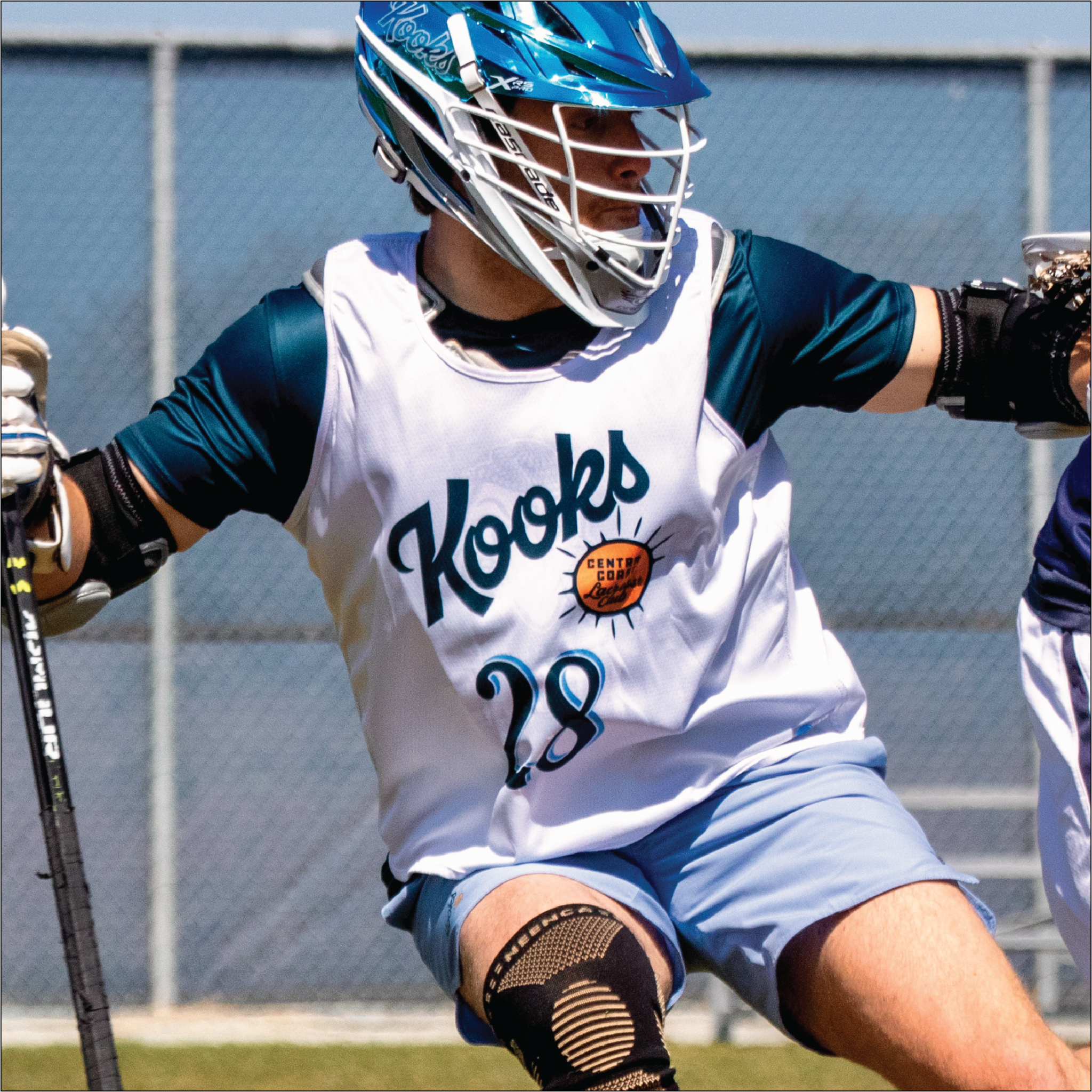 Person playing lacrosse wearing a 'Kooks' jersey with number 28 on a sports field.